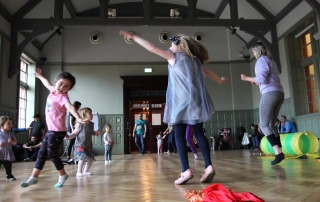 Image is a photograph of children dancing around the Grand Hall of the Whitworth Art Gallery