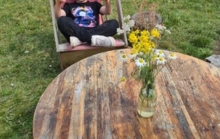 A happy boy is sitting on a lounger and showing two thumbs up, while at the Platt Fields Market Garden.