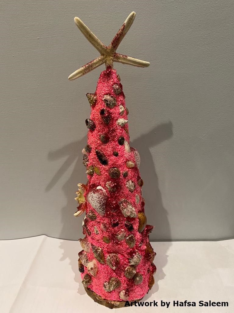 Photo of a handmade red Christmas tree made of sand, shells and glitter. The text at the bottom-right reads 