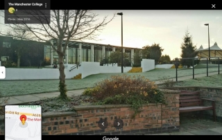 This screenshot of a photo at The Manchester College's Openshaw Campus shows the main building, the grassy lawn out front, and some gazebos to the side.