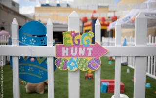 The photo shows a fenced area for an Easter Egg Hunt. In the middle of the fence is a colourful sign that says "EGG HUNT".