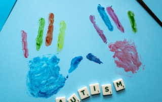 Scrabble tiles spelling the word Autism are laid on top of a blue sheet that has colourful handprints on it.