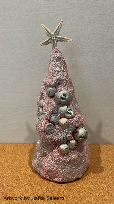 Photo of a handmade red Christmas tree made of sand, bells and glitter. The text at the bottom-left reads 