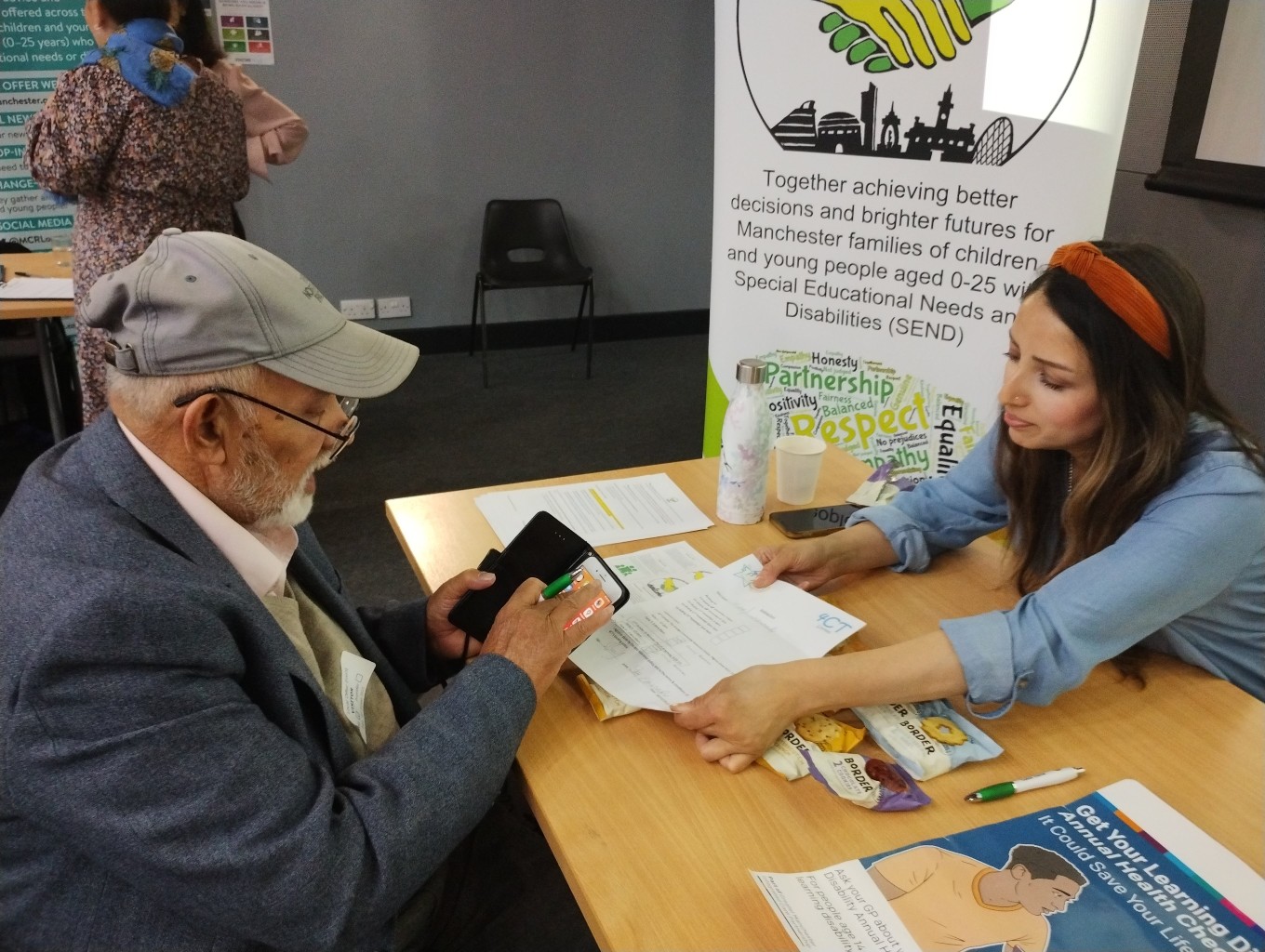 The photo shows Jen from the MPCF team speaking to a Drop-in visitor, with the forum banner behind her, at the Local Offer Drop-in @ Manchester College's Openshaw campus back in October 2023.