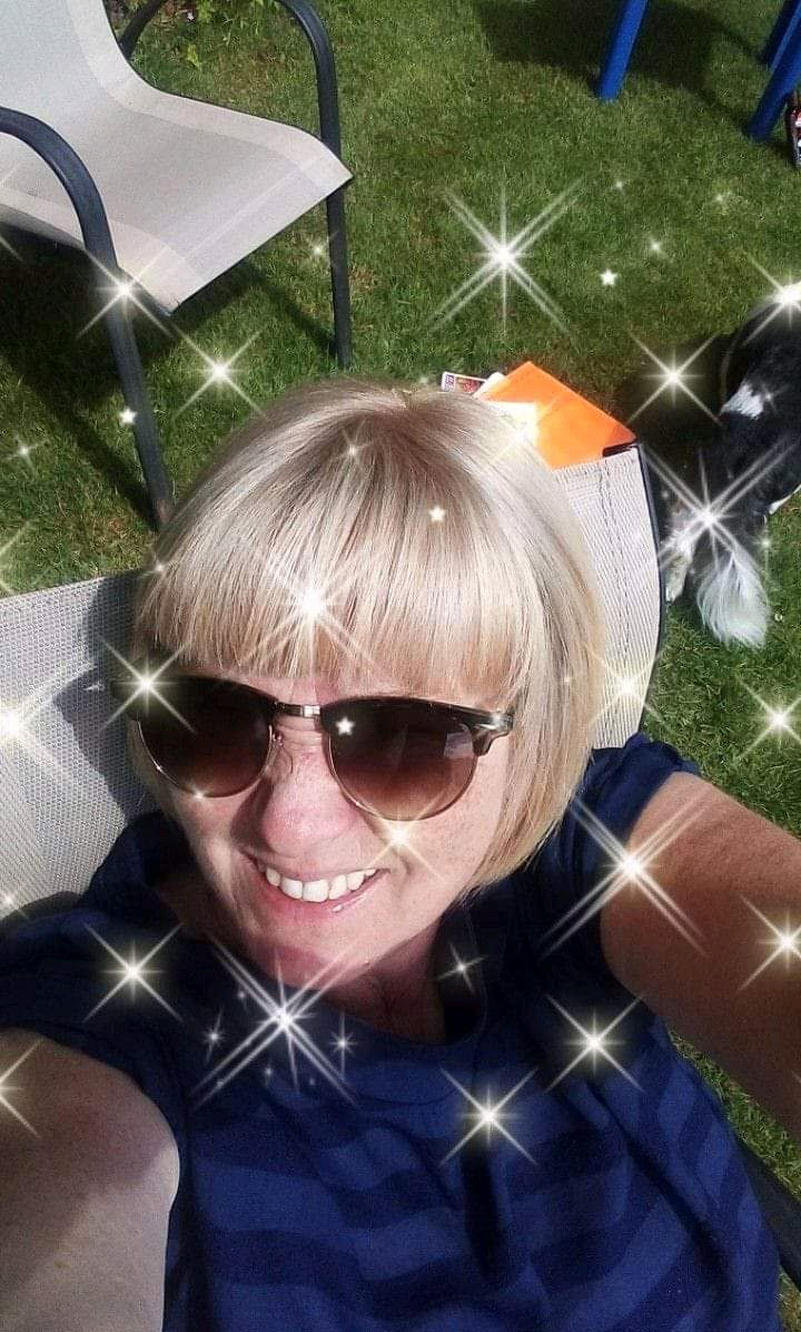 Image is a photograph of Karen, sat in a garden, looking up to the camera and smiling, with a twinkling star effect applied to the photograph