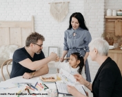 A man gives a fistbump to his daughter while the mum and a social worker looks on. In front of them is a table filled with paper and coloured pens, among other things.