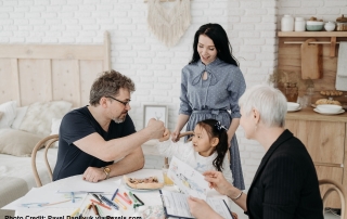 A man gives a fistbump to his daughter while the mum and a social worker looks on. In front of them is a table filled with paper and coloured pens, among other things.