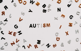 Various letters of different colours randomly arranged surrounding the word 'AUTISM'