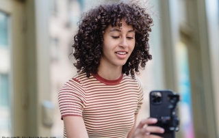 A woman with curly hair wearing a red striped shirt is taking a selfie.