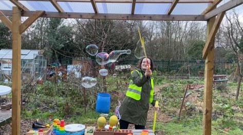 Photo shows Sian from Manchester Bees Forest School waving a big bubble wand