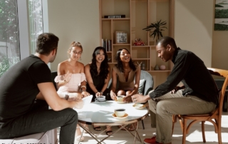 The photo shows two men and three women of different ethnicities chatting and having a brew together.