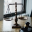 The photo shows a balancing scale ("scales of justice") in the middle and a gavel on the lower right hand side.