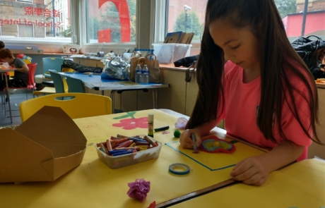 The photo shows a girl enjoying her arts and crafts while other families enjoy the Relaxed Creative Session at Manchester Art Gallery in summer 2023.